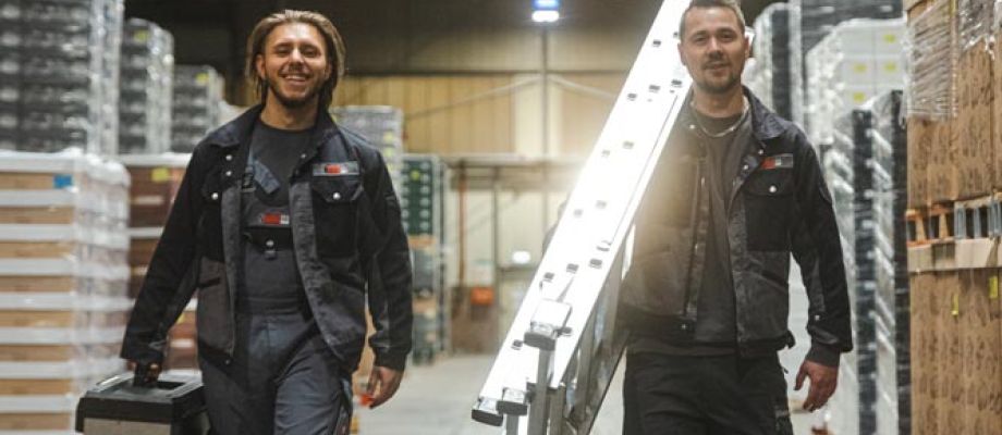 2 Mitarbeiter in einer Halle mit Leiter und Werkzeugkoffer in der Hand.
