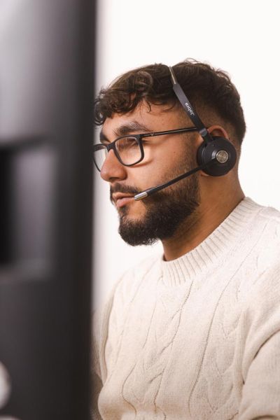 Ein Mann mit Brille und kurzem Bart trägt ein Headset und arbeitet konzentriert an einem Computer.